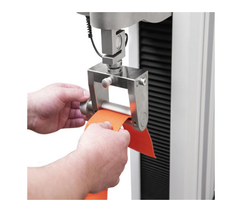 To load the sample, (1) insert the material through the slot, then (2) turn the dial to wrap the material around itself, then (3) insert the anchor pins (not pictured).